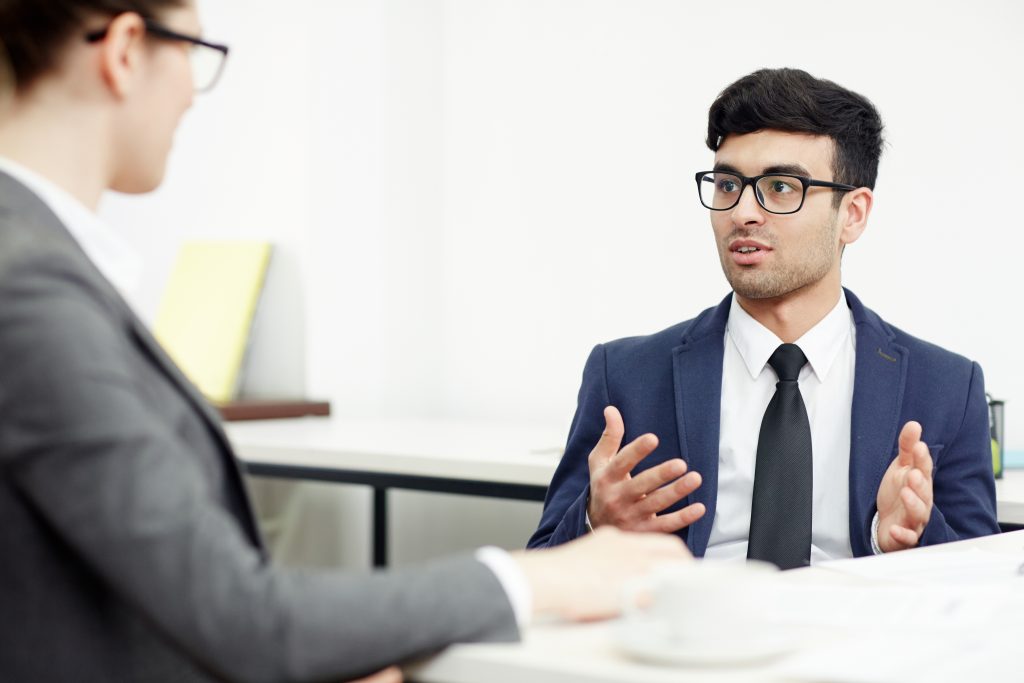 Portrait of young bearded entrepreneur conducting negotiations with business partner while sitting at table in spacious boardroom
