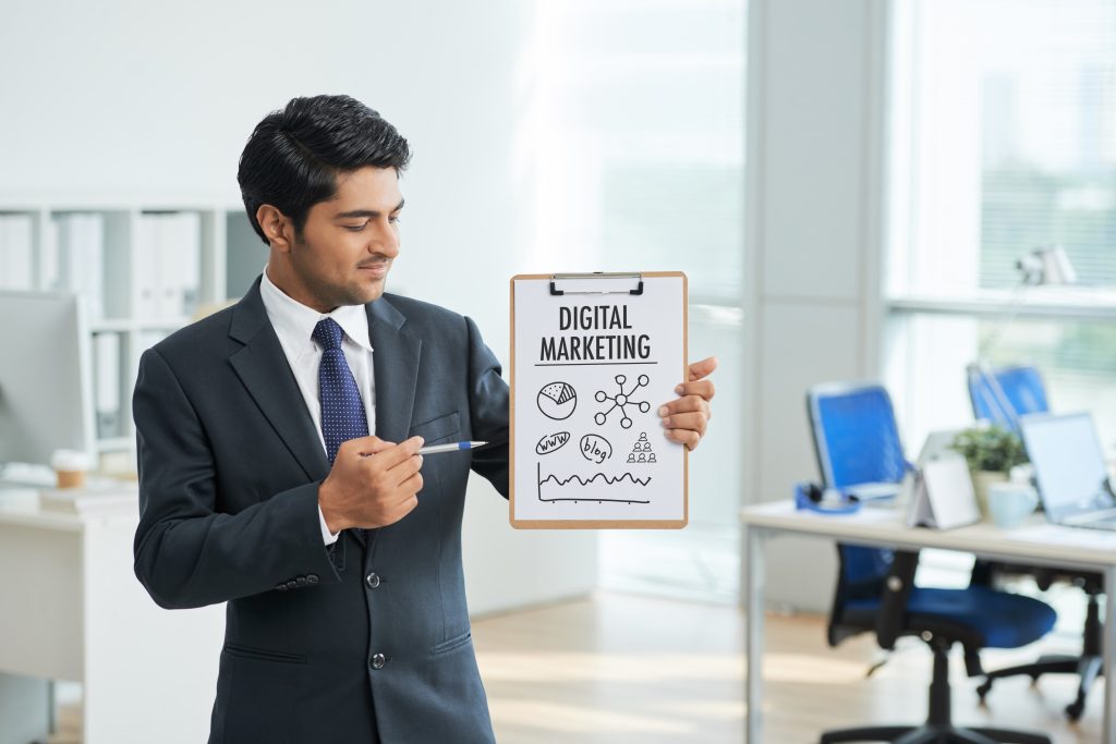 man-suit-standing-office-with-clipboard-pointing-poster-with-words (1) learn digital marketing steps